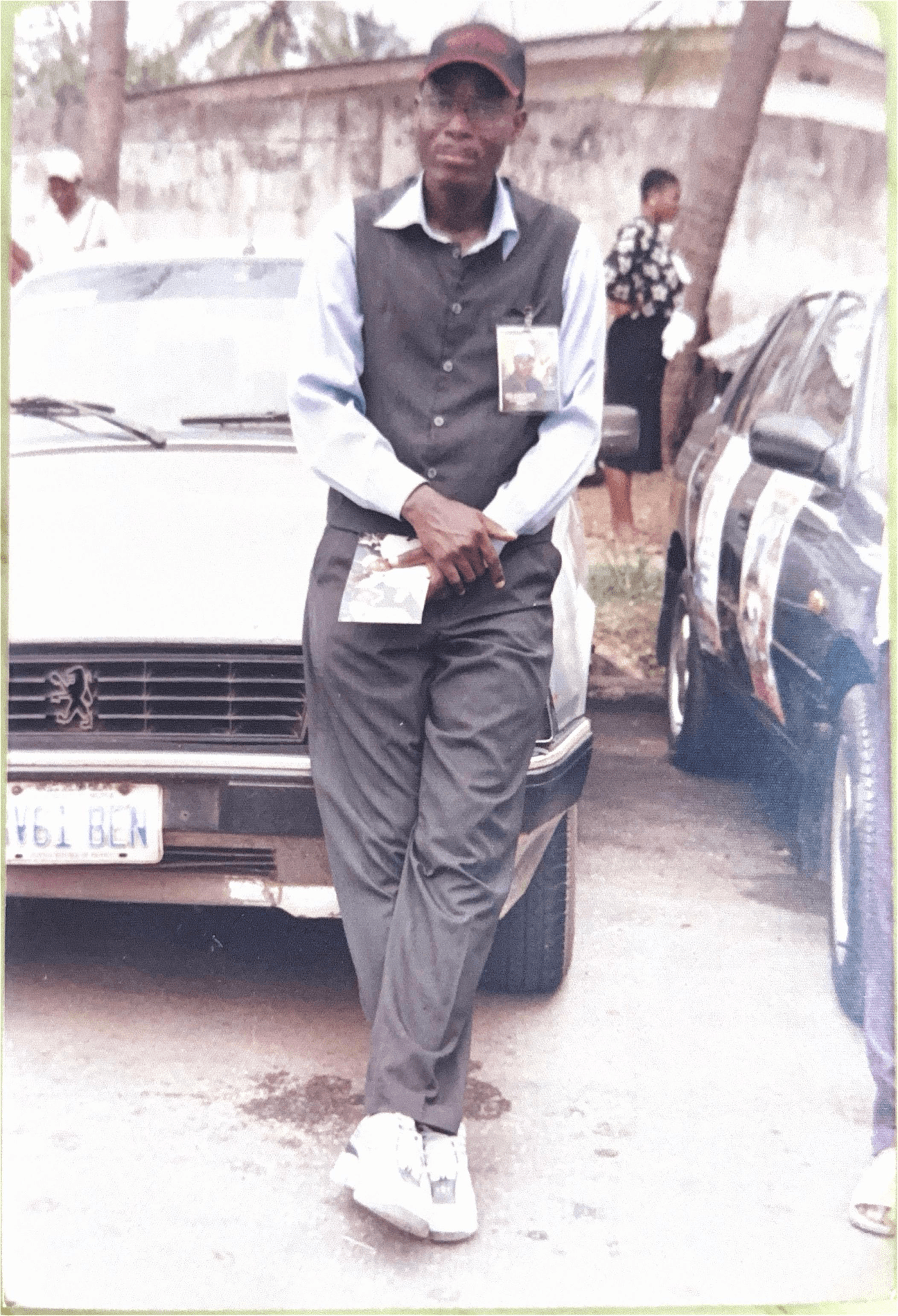 A younger Comrade Ayeola leaning against a vintage Peugeot, badge on chest